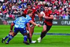 Rugby: a player carries the ball forward while the other team tries to tackle him.