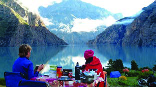 Travellers having a meal beside a still mountain lake. To talk about a place like this, say where it lies and how a visitor can reach it.