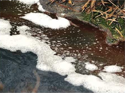 Pollutants produced from an industry: foam and dark, coloured waste water flowing into a stream.