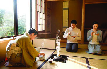 At a Japanese tea ceremony the host prepares tea with careful, practised movements while the guests kneel.