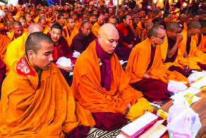 Buddhist monks in saffron robes chant together at a prayer ceremony.