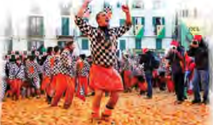 A thrower in a checked costume raises his arms in a square carpeted with crushed oranges.