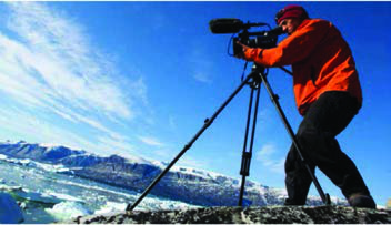 Balog filming from a rocky shore with icebergs behind him: twenty five cameras like this one, housed in protective units, watched the glaciers for three years.